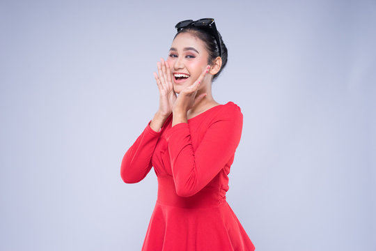 An attractive woman wearing casual red attire with gestures and poses towards copyspace isolated on grey. Good for technology, transportation, business or finance concept