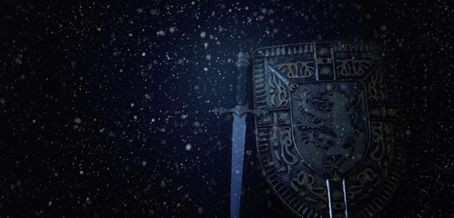 photo of shield knight armor and sword in the falling snow over dark background. Medieval period...