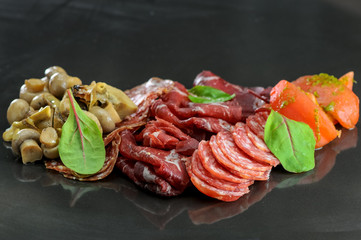 cold cuts of sausages and jamon with fish on a black glossy background
