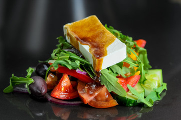 salad with olives tomatoes arugula and cheese from the chef on a black background