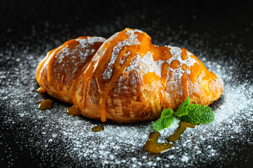 croissant watered with caramel sprinkled with powder and decorated with mint on a black background