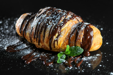 croissant peel with chocolate and sprinkled with powder decorated with mint on a black background