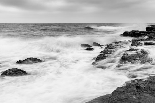 Black and white photo of the ocean with water flowing across rocks