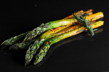 grilled asparagus on a black background with a sprig of rosemary