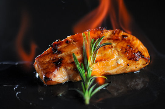 grilled fish fillet on a black background with a sprig of rosemary with fire