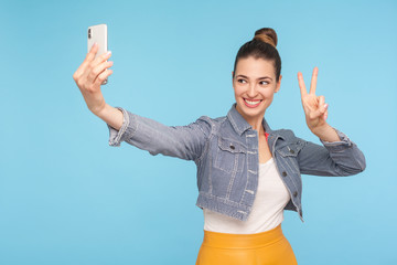 Attractive happy woman with hair bun in fashionable outfit showing victory or peace gesture while...