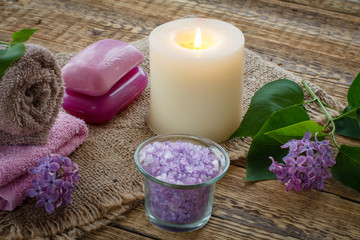 Fototapeta na wymiar Towel, soap, candle and lilac flowers on wooden background.