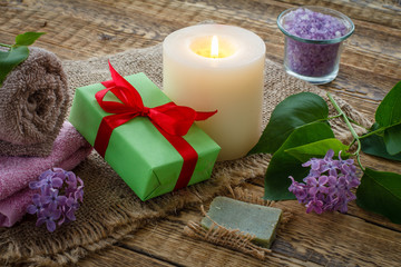 Towels, gift box, candle and lilac flowers on wooden background.