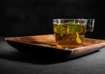 Mint tea with leaves in glass cup on black background