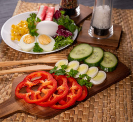 Salad plate on the table with wooden cutlery. Crab sticks, boiled egg, corn, paprika and greens