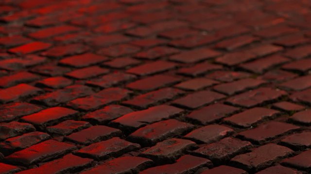 Close up of a brick road illuminated with red light, showing vehicles passing over it