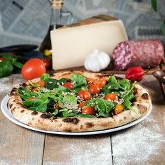 Fototapeta na wymiar Italian style pizza, fresh arugula and cherry tomatoes prepared on wooden boards