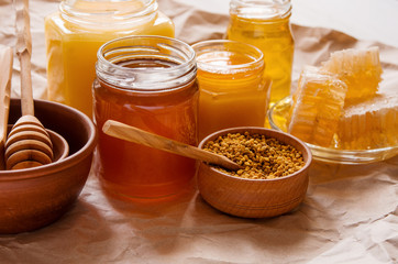 Liquid yellow bee honey in glass jars, pollen and honeycomb on Kraft paper on table