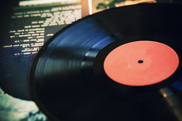 An old vintage black vinyl record lies on the cover of a music album with the playlist's text on it.