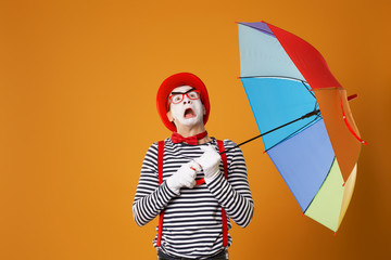 Mime looking up with multi-colored umbrella isolated on empty orange background