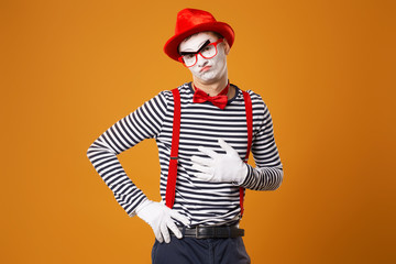 Mime clown in red hat and in vest pointing on orange background