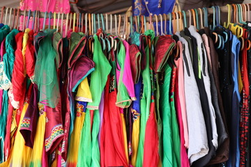 close-up of pink, red yellow orange, purple, pink, and many designs men and women modern dresses hanging on wood rod in market for sells,