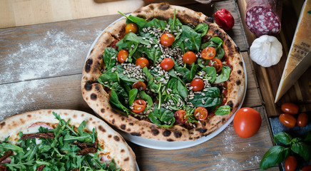 Italian style pizza, fresh arugula and cherry tomatoes prepared on wooden boards