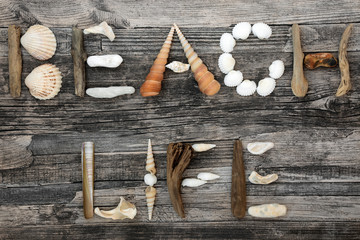 Seashell, driftwood and pebble abstract composition forming the word beach life on rustic wood background. Summer holiday concept.