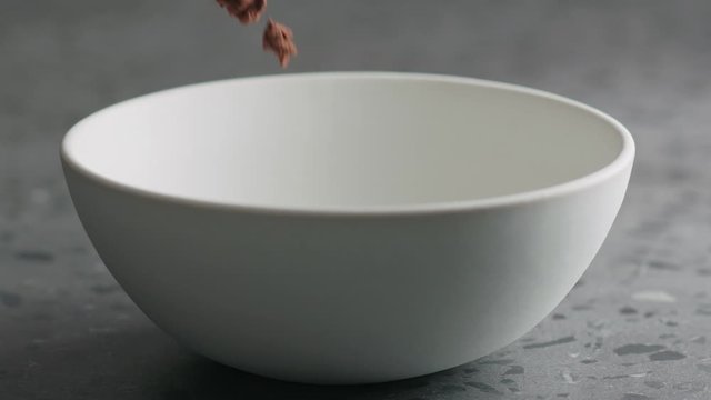 Slow motion chocolate granola fall into white bowl on terrazzo surface