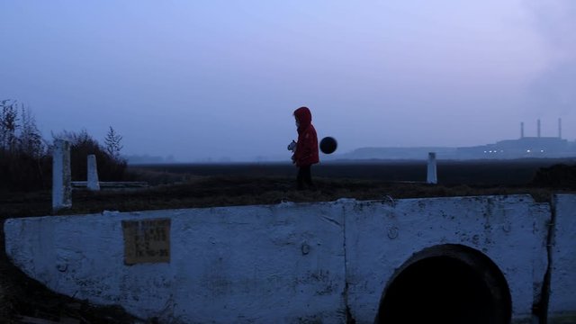 Bridge child in a respirator red jacket with a toy and a black ball, from behind the factory, radiation fear and the apocarypse, hopelessness