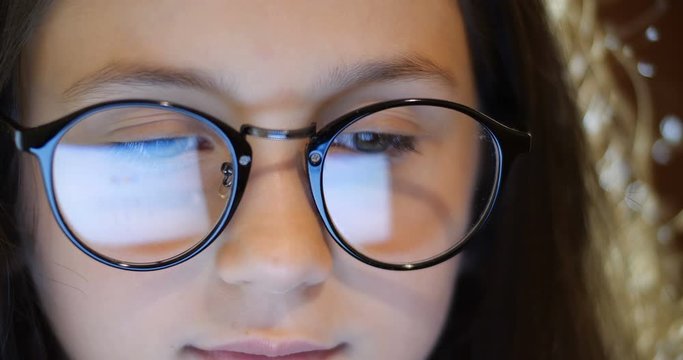 Close up  portrait of smart schoolgirl with long brown hair wearing  glasses. Girl  using computer. Laptop screen reflect  in glasses. Concept of eye fatigue and ophthalmic problems. Slow motion