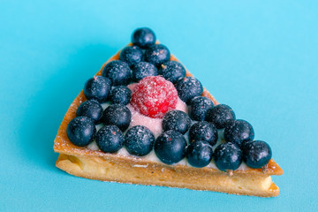 Piece of berry pie with blueberries and raspberries on a blue background