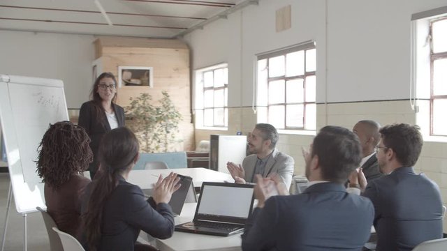 Colleagues applauding after presentation. Smiling office employee standing near whiteboard. Business meeting concept