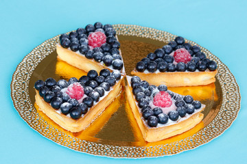 Pieces of berry tart on a gold plate on a blue background