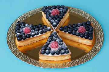 Pieces of berry tart on a gold plate on a blue background