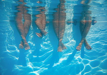 Close up of friends, family legs underwater in the swimming pool with copy space - obrazy, fototapety, plakaty