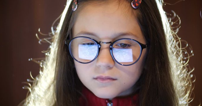 Portrait of smart schoolgirl with long brown hair wearing  glasses. Girl using computer. Laptop screen reflect  in glasses. Concept of eye fatigue and ophthalmic problems. Slow motion 50 fps