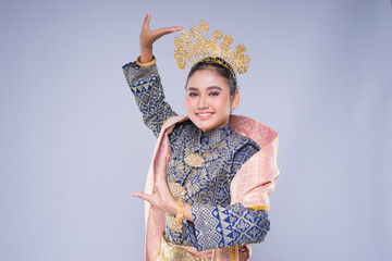 A beautiful Malaysian traditional female dancer with a charming smile performing a cultural dance steps in a traditional outfit. Half length isolated in grey.