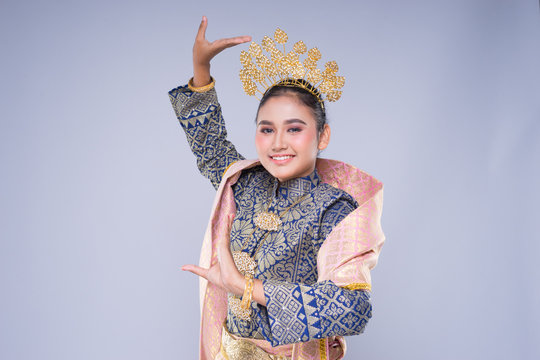 A beautiful Malaysian traditional female dancer with a charming smile performing a cultural dance steps in a traditional outfit. Half length isolated in grey.