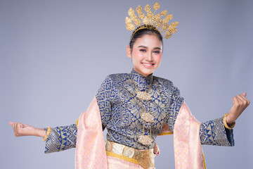 A beautiful Malaysian traditional female dancer with a charming smile performing a cultural dance steps in a traditional outfit. Half length isolated in grey.