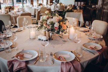 the festive table is decorated with compositions of flowers and greenery, on the table there are candles, glasses, plates and cutlery