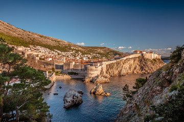 Medieval fort of Old Town of Dubrovnik with round tower inside ancient brick walls, Croatian flag on the top, blue sea with promontories on foreground