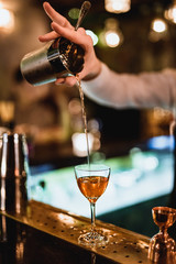 Pouring a drink from a shaker through a strainer into a cocktail glass. Selective focus. Vertical lifestyle image. High ISO.