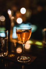 A dark lifestyle image of a cocktail in a nick and nora glass at the bar, bokeh lights, high iso, film grain effect