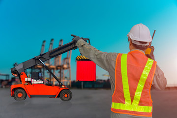 worker in port hand holding walkie talkie finger pointing forklift handling container box loading to truck in import export logistic zone.