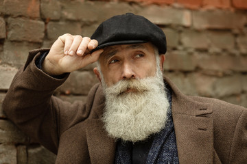 Fashionable senior man with gray hair and beard is outdoors on the street.