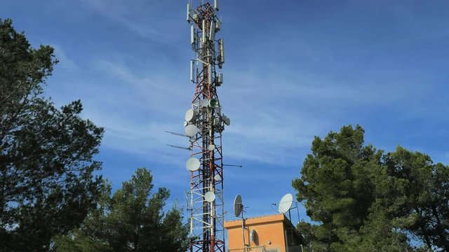 Modern tower with huge complex of telecommunication antennas on old bricks house hidden in pine trees.  Mountain trail over Pintal Vermell peak, Mallorka island, Spanish  Balears islands.