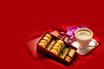 Eastern sweets. Baklava in a red box, a cup of coffee and an orchid branch on a red background. Baklava still life