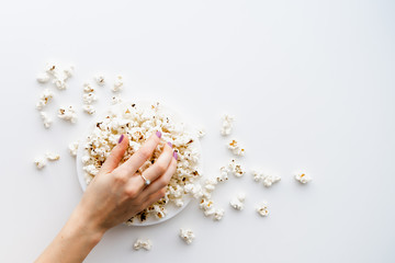 Woman's hand taking popcorn from a plate. White background, top view. Movie and pastime concept.