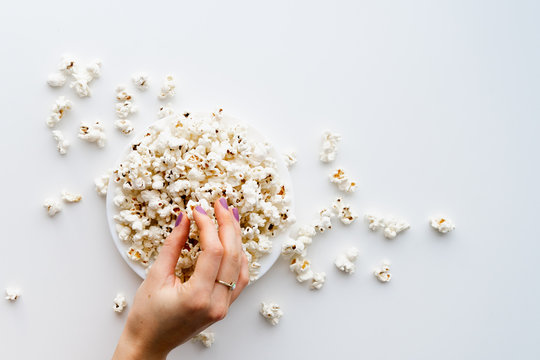 Woman's hand taking popcorn from a plate. White background, top view. Movie and pastime concept.