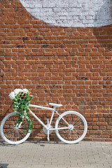 Fototapeta na wymiar White decorative old bike with a basket of flowers against a brick wall. Copy space