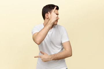 Portrait if active energetic young man having fun making gestures as if holding pistol. Handsome dark haired guy dancing against white blank studio wall background with copy space for your information