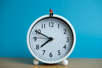 Miniature people for morning reading time concept - young man seating above clock reading a book