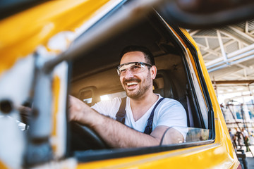 Smiling handsome unshaven worker driving vehicle on construction site.