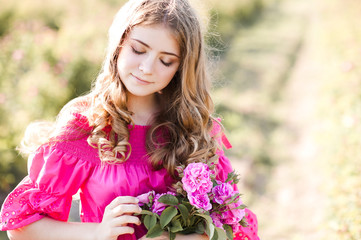 Smiling teen girl 16-17 year old with blonde long curly hair holding fresh pink roses posing in...